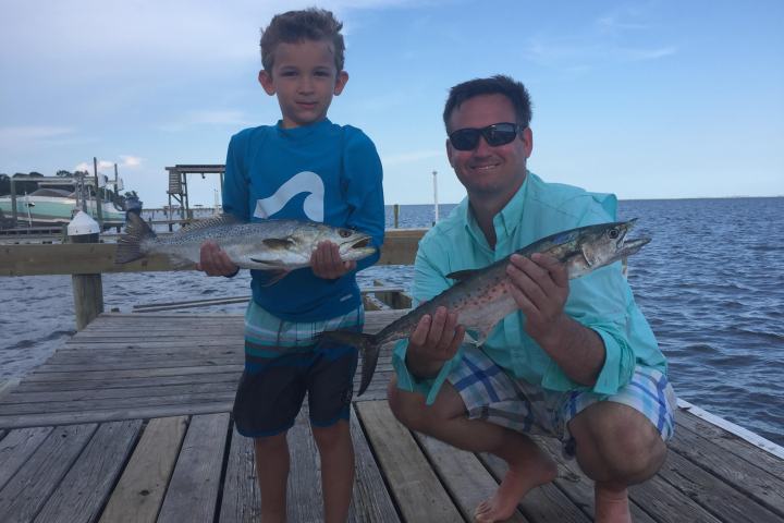 Man and young boy both holding up fish caught on fishing trip