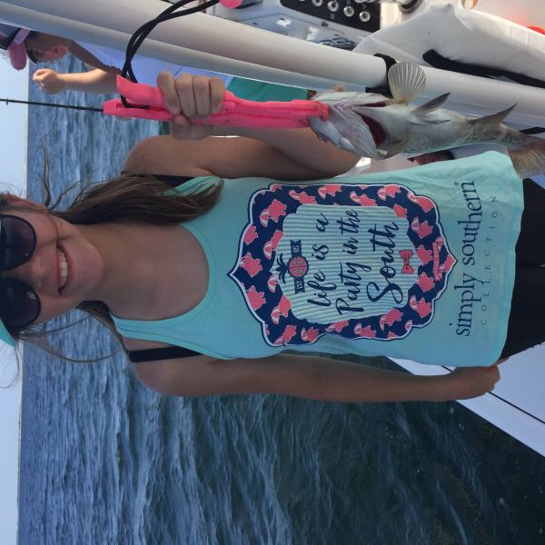Girl holding up silver fish while standing on a boat