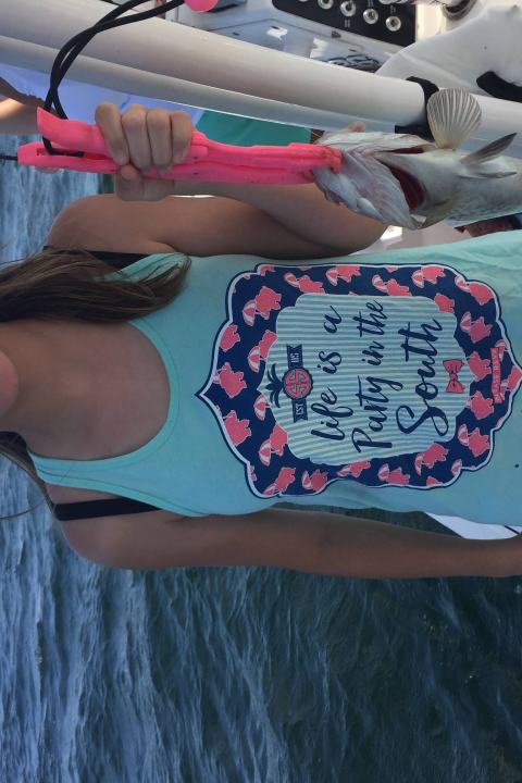 Girl holding up silver fish while standing on a boat