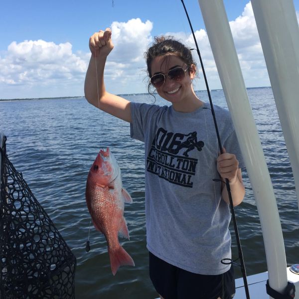 Girl holding up red snapper while standing on a boat