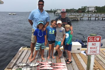 Group of kids standing with adult with fish at their feet on pier