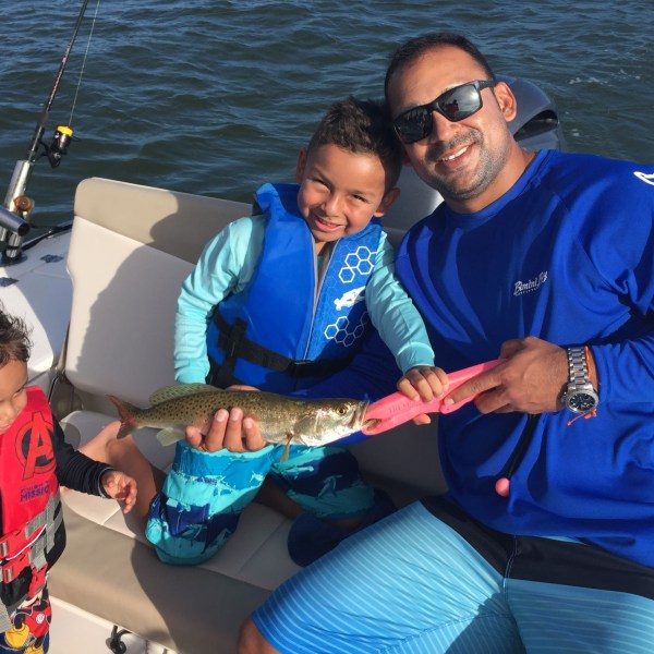 Man with his children smiling at camera on the boat while holding a fish