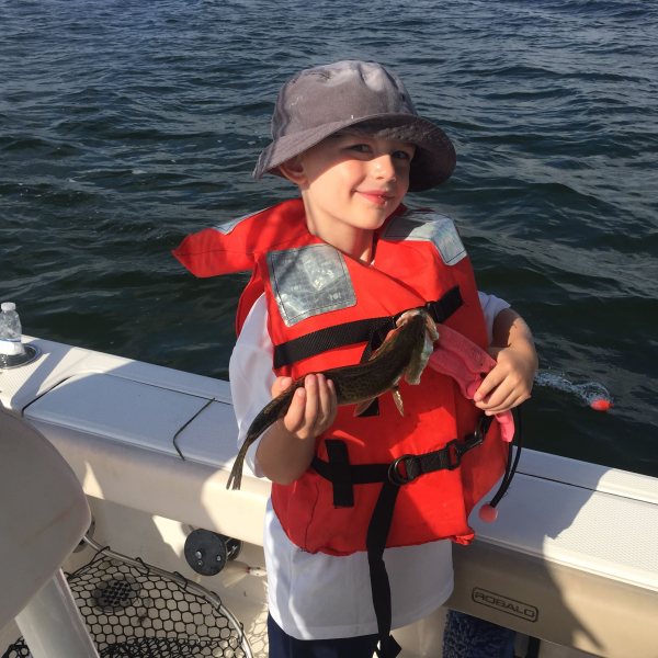 Little boy holding small fish he caught on the boat