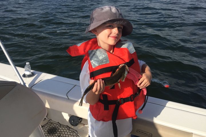Little boy holding small fish he caught on the boat