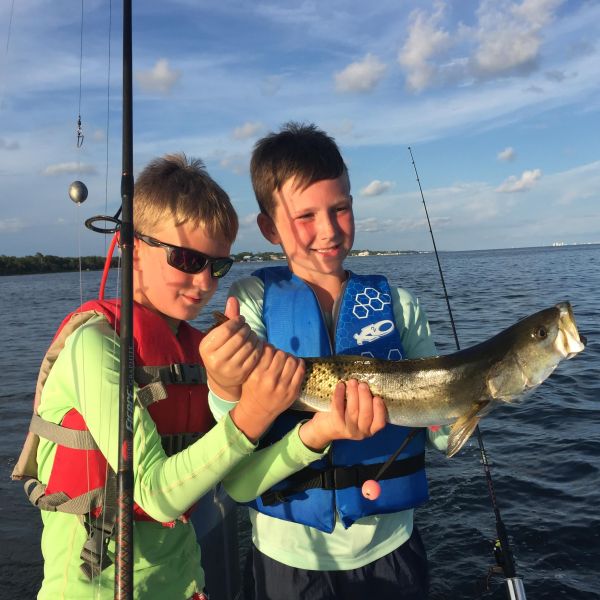 Two young boys holding fish up on the boat