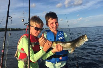 Two young boys holding fish up on the boat