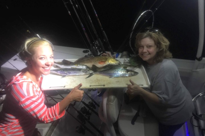 two women leaning together around fish caught on boat