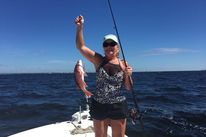 Woman holding up red snapper on bow of boat