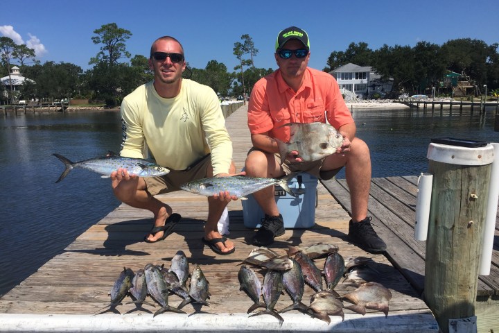 Two men crouching down by fish caught on fishing charter