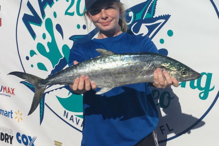 Woman holding up Spanish Mackerel on front of fishing contest sign