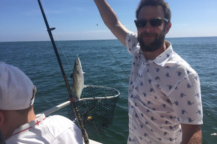 Man holding up mackerel fish he just caught on the boat